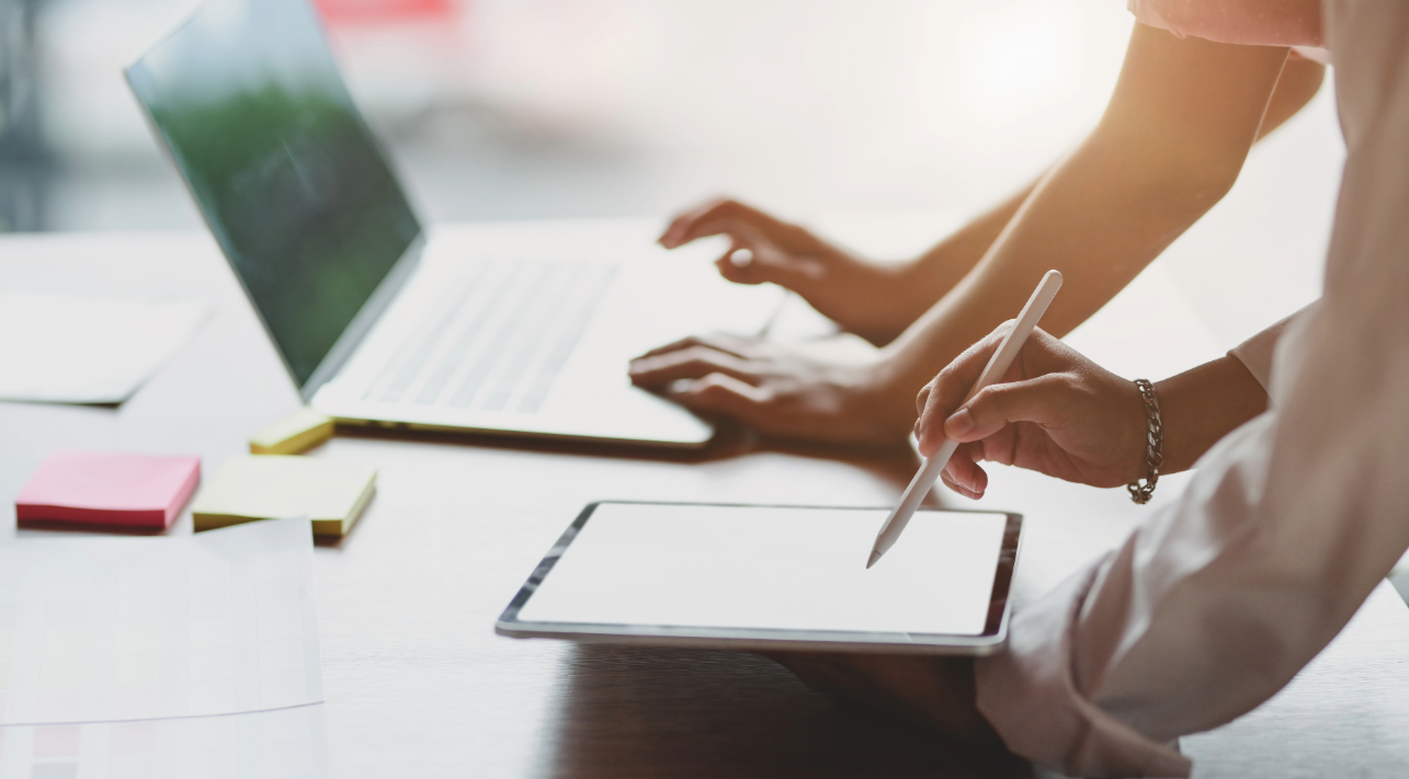 Image of two people sharing information, plans and ideas using a laptop and tablet.